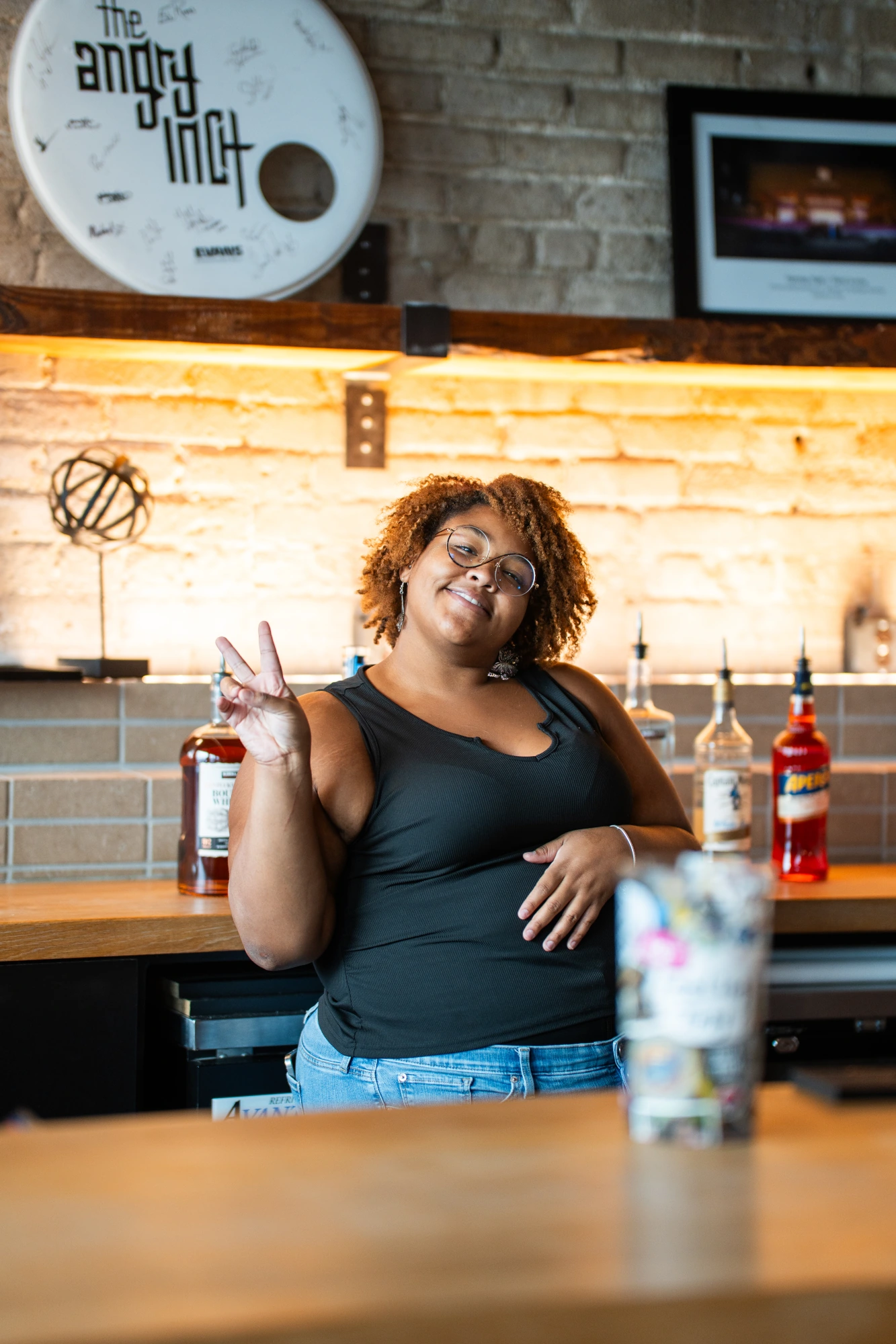 A smiling bartender throwing a peace sign behind the bar